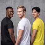 Three men standing side by side wearing plain athletic t-shirts in black, white, and yellow, photographed against a textured gray concrete wall.